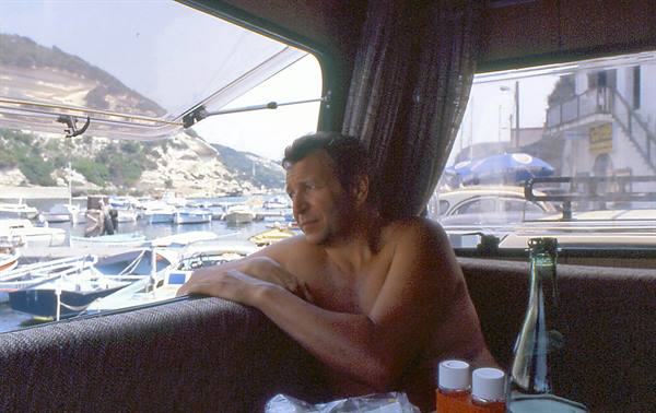 Shirtless man inside a camper overlooking a harbor full of boats