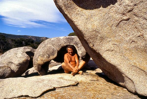Man sitting in the shade of huge granite boulders, blue sky above