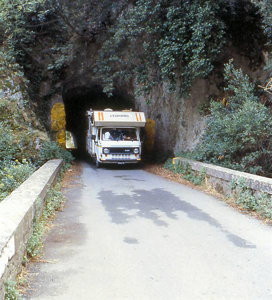 White Leopard camper van exiting a rock-cut tunnel on a stone-walled road
