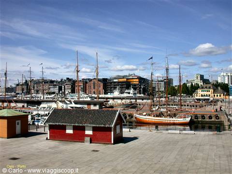 Oslo harbor: red wooden cabin, moored tall ships and city under blue sky