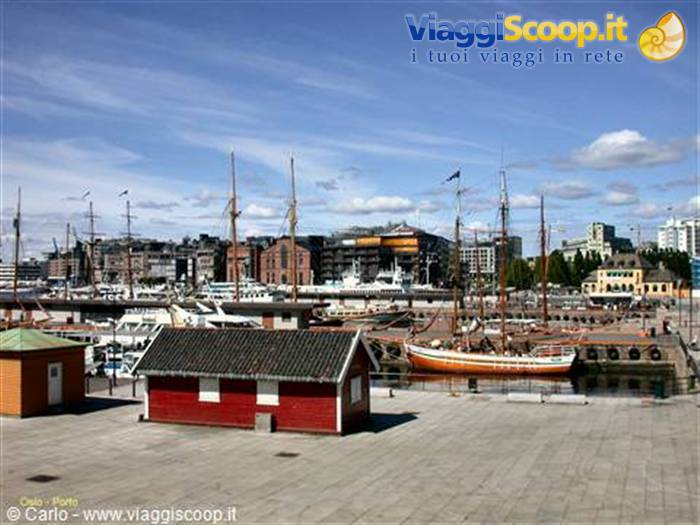 Oslo harbor: red wooden cabin, moored tall ships and city under blue sky