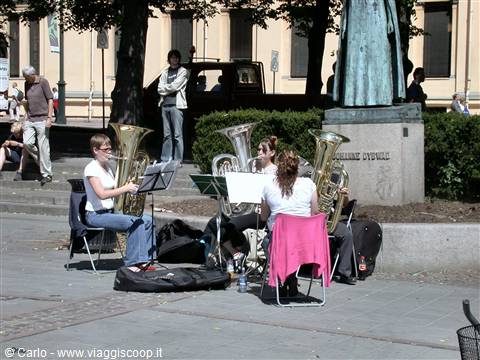 Musicians playing tubas on chairs in a sunny city square