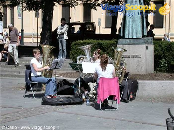 Musicians playing tubas on chairs in a sunny city square