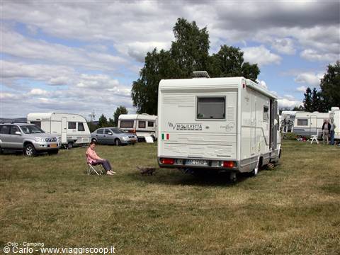 White motorhome and woman sitting at Oslo campsite among caravans and trees