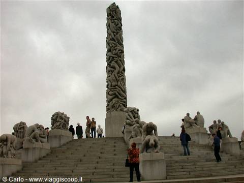Granite monolith with intertwined figures in Oslo's Vigeland Park, visitors among statues