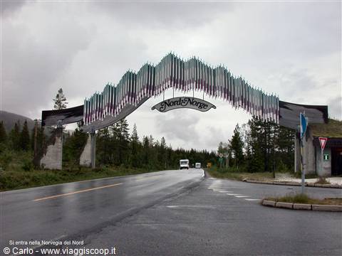 Metal arch reading Nord-Norge over the wet road, cars passing beneath a grey sky