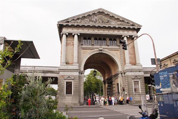 Tourists cross the street under the monumental stone arch of Porta Galliera, Bologna