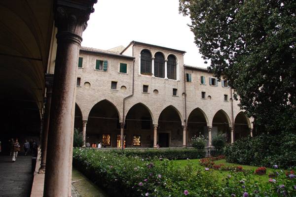 Cloister with arched arcade, stone columns and flowering garden in Ravenna