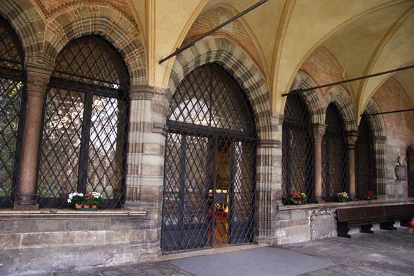 Cloister arcade with bichrome stone arches, wrought-iron grilles and flowers on sills