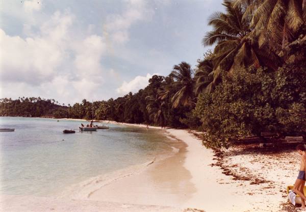 Boats on white sand beneath palms, turquoise sea and clouds