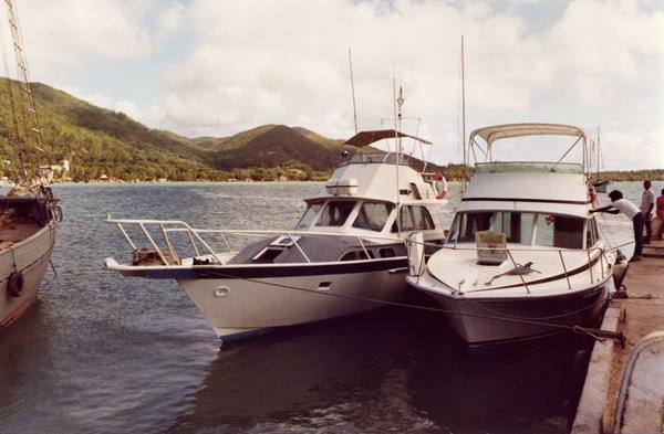 White motorboats moored at the dock, a man tying ropes, green hills behind