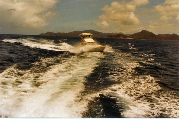 White speedboat cutting through dark waves, green islands under clouds