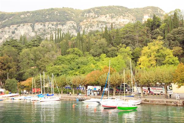 Green sailboat moored at the harbor, rocky mountains and autumn trees on Lake Garda