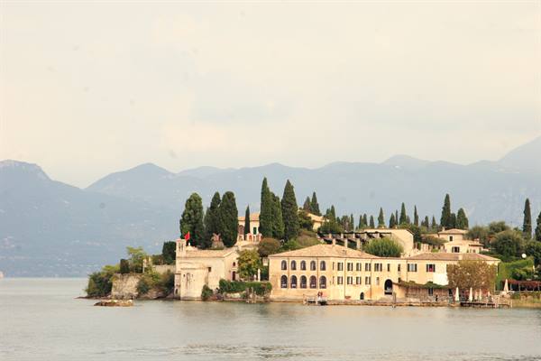 Historic villa with cypresses on Isola di Garda amid mist and mountains