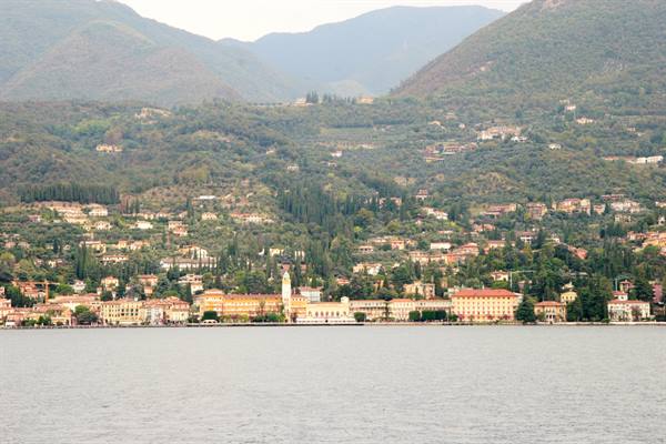 Lakeside promenade with colorful buildings and bell tower on Lake Garda, forested mountains behind