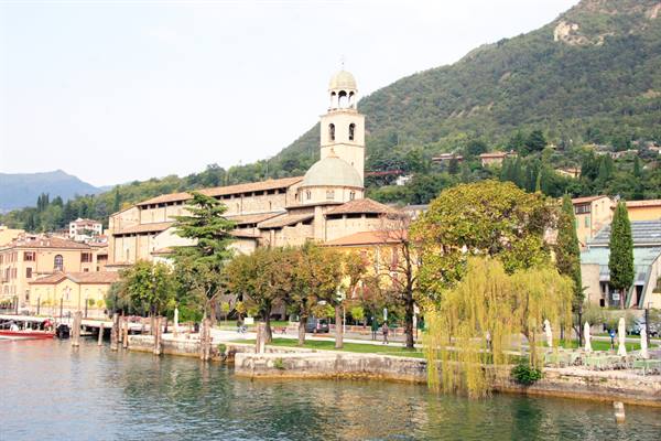 Salò cathedral by the Garda lakeside promenade among trees and green mountains