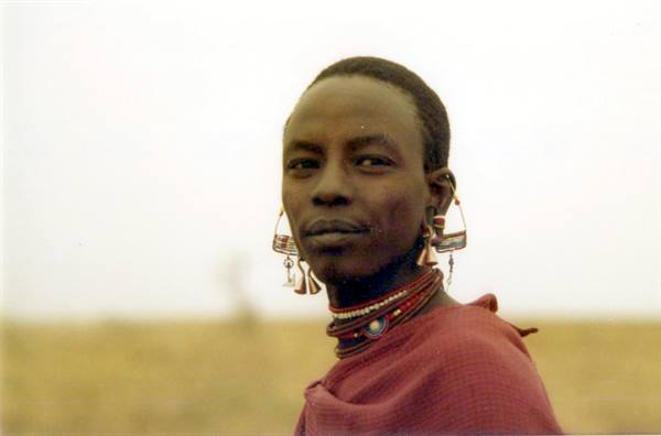 Young Maasai man wearing beaded earrings and red necklaces, gazing at camera