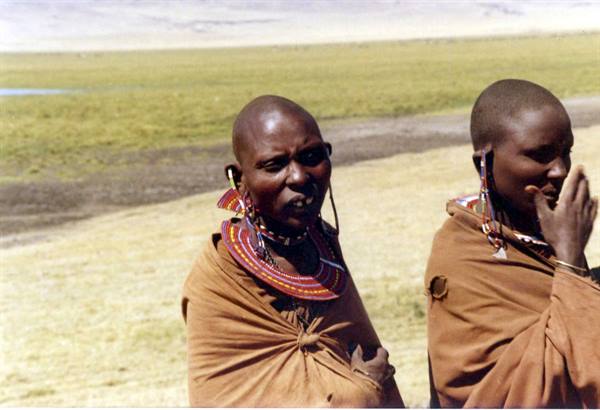 Maasai women wearing beaded necklaces and earrings, draped in ochre cloth