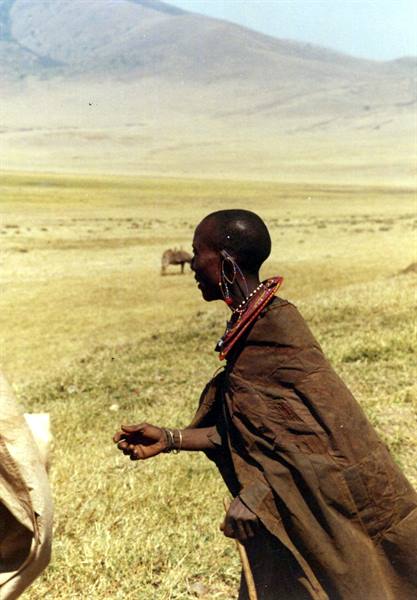 Maasai woman wearing beaded necklace and earrings walks across dry savanna