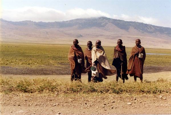 Five Maasai in ochre cloths walk across the Ngorongoro savanna
