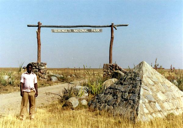 Man in pink shirt standing by the wooden Serengeti National Park gate