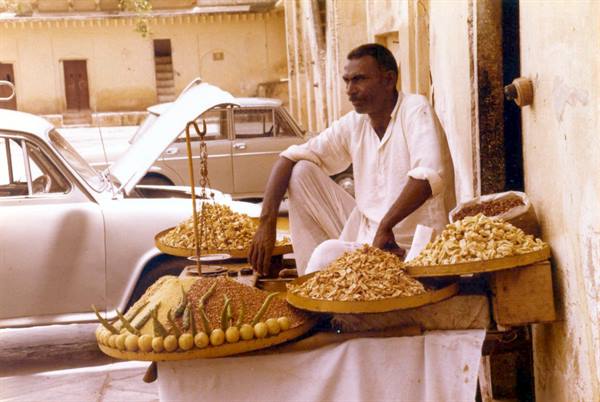 Vendor seated beside trays of dried fruit and spices, India