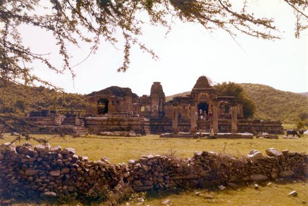 Ancient stone temple among hills, people at entrance, low stone wall foreground
