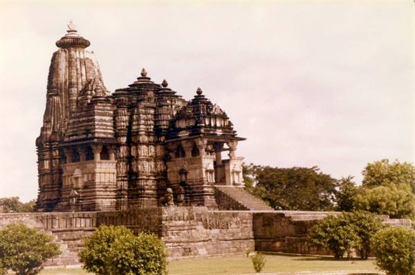 Carved stone temple at Khajuraho, curved tower, morning light, green trees