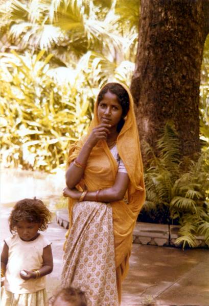 Woman in yellow sari with child under palm trees, India