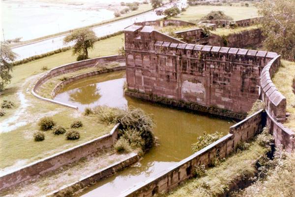 Sandstone walls and green moat of Agra Fort under soft light
