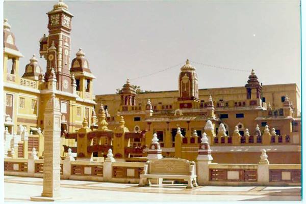 Yellow and brown temple complex with clock tower, paved courtyard