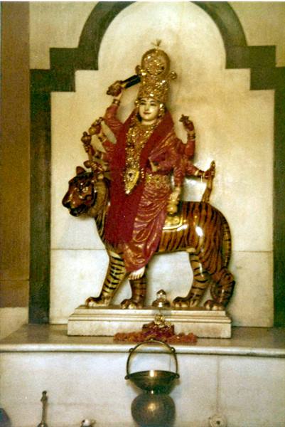 Durga statue riding a tiger inside a Hindu temple, with offerings below