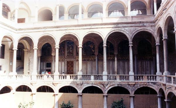 Courtyard with three-tiered arches, marble columns, sunlight, visitors along the balustrade