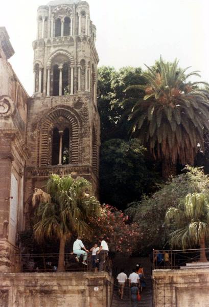 Medieval stone bell tower in Palermo, tourists on steps among palm trees