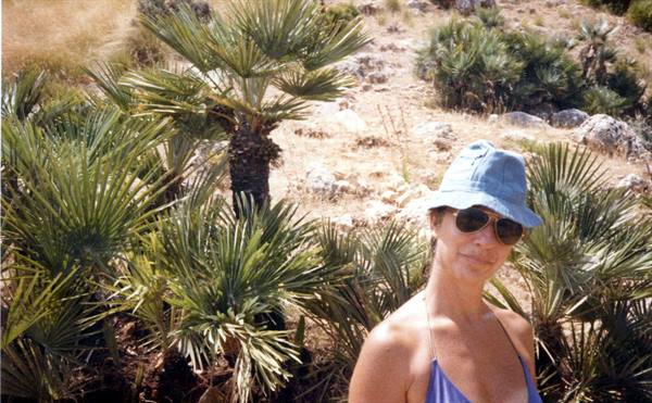 Woman in blue hat and sunglasses among dwarf palms and rocks