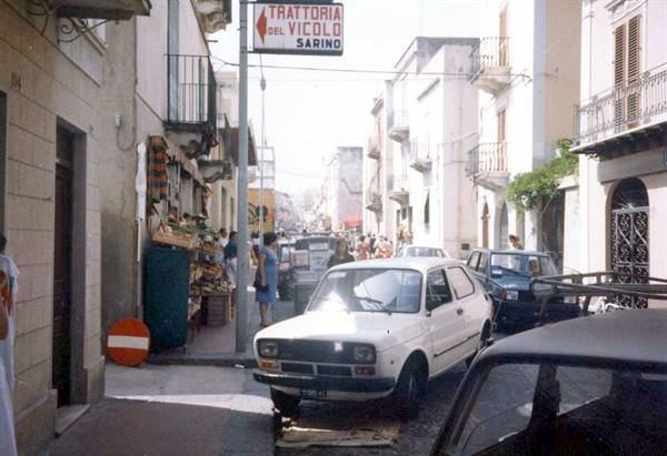 Cars parked on busy street, trattoria del Vicolo Sarino sign, whitewashed buildings
