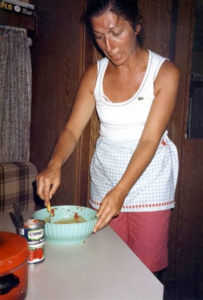 Woman in white tank top and checkered apron mixing in a green bowl in a kitchen