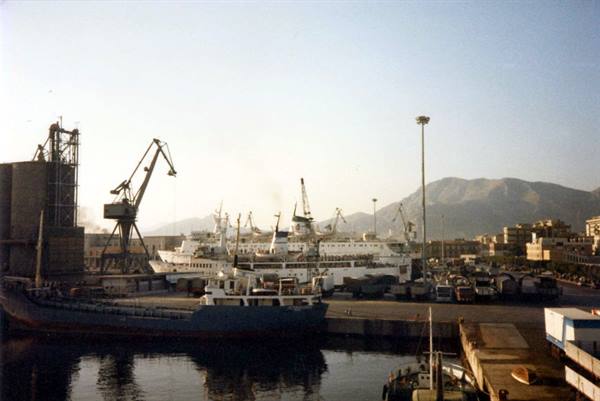 Cargo ships and ferries docked at the harbor, cranes and mountain behind