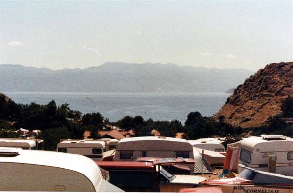 Caravans and campers at a campsite facing the sea and hazy mountains