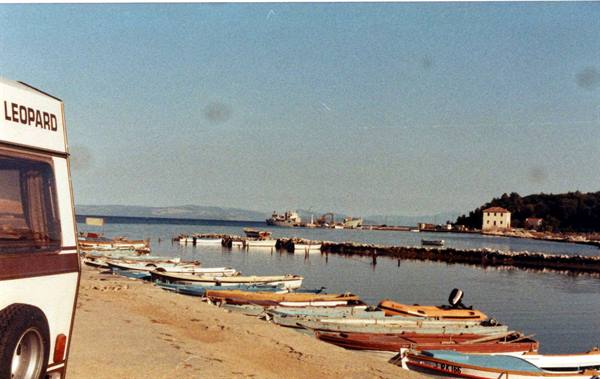 Leopard camper van on the beach with colorful boats moored near the pier