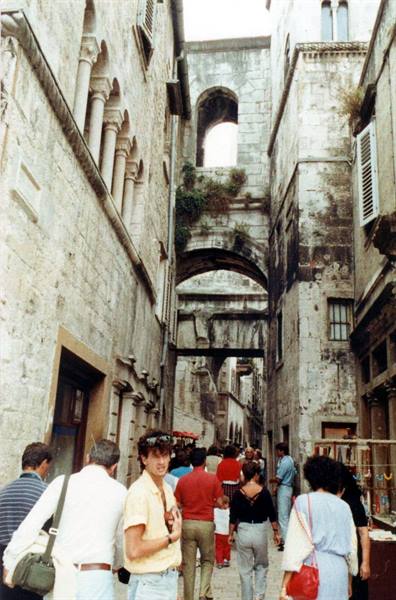 Tourists walk through a narrow stone alley with ancient arches in Split
