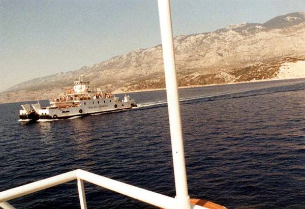 White ferry loaded with passengers sails past sunlit rocky mountains