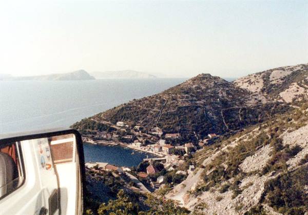 Camper mirror in foreground, small seaside village below dry hills