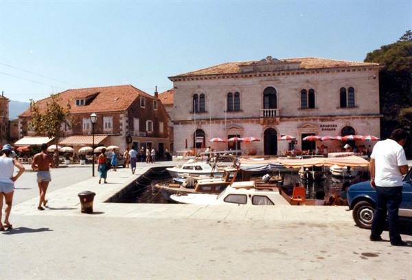 Hvar harbor: boats, stone building and tourists under sunny sky