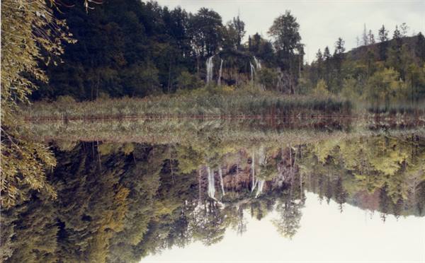 Waterfalls among autumn trees and reeds, mirrored in still water at Plitvice