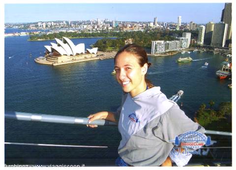 Smiling girl on Sydney Harbour Bridge railing, Opera House and skyscrapers behind