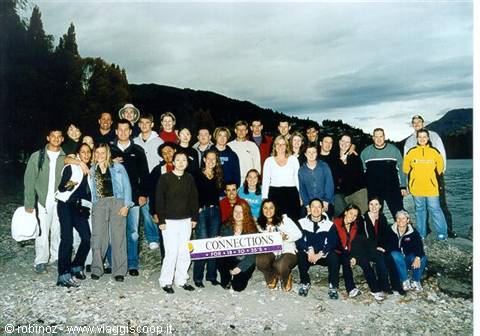 Tour group holding Connections banner on pebbly lakeshore under cloudy sky