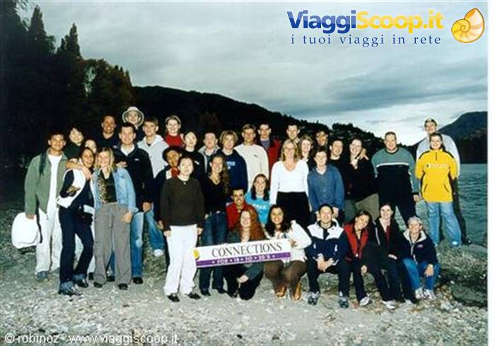 Tour group holding Connections banner on pebbly lakeshore under cloudy sky
