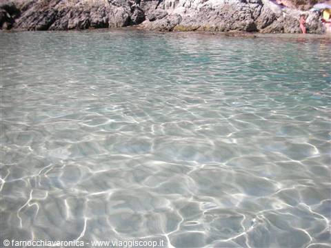 Clear water with light reflections on the sand, rocks behind
