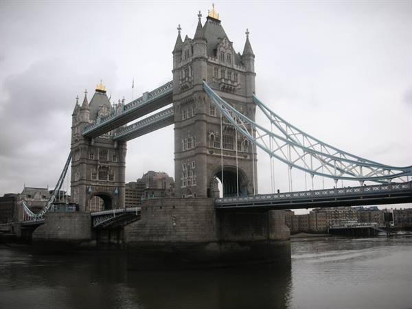 Tower Bridge in London, stone towers and white suspension cables under grey sky